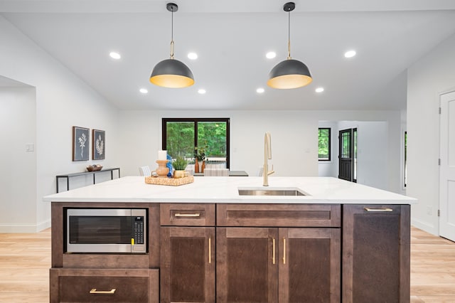 kitchen with hanging light fixtures, light wood-type flooring, dark brown cabinetry, a kitchen island with sink, and sink