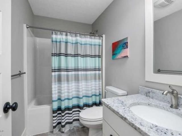 full bathroom with shower / tub combo with curtain, vanity, and toilet