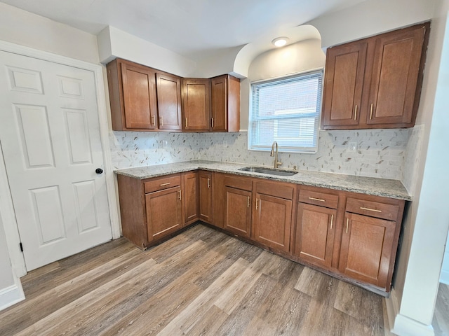 kitchen with decorative backsplash, wood-type flooring, light stone countertops, and sink