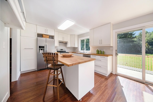 kitchen with white cabinets, a kitchen bar, butcher block counters, and stainless steel appliances