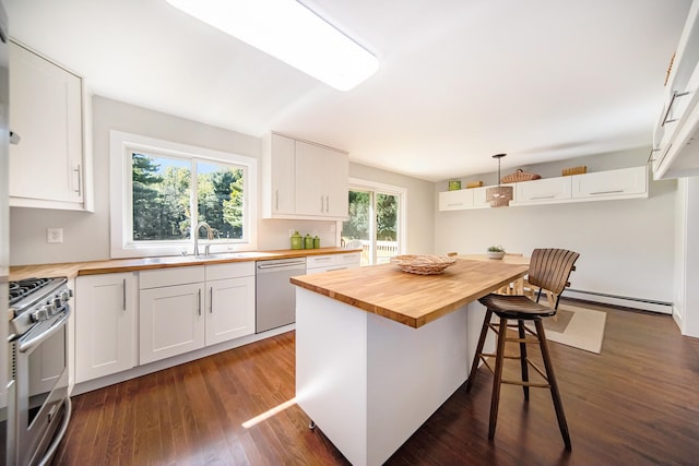 kitchen featuring wood counters, stainless steel appliances, a baseboard radiator, white cabinetry, and a breakfast bar area