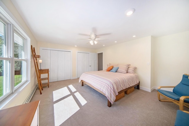 bedroom featuring multiple closets, light colored carpet, ceiling fan, and a baseboard heating unit