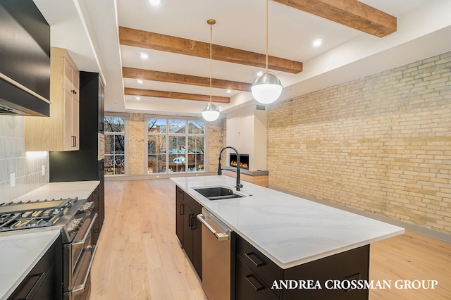 kitchen featuring sink, an island with sink, stainless steel appliances, pendant lighting, and brick wall