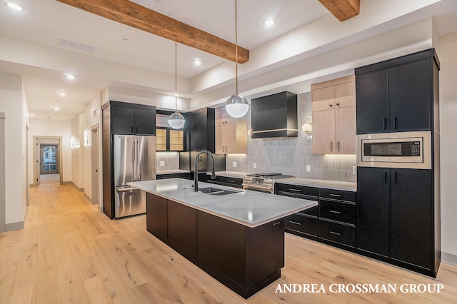 kitchen featuring hanging light fixtures, an island with sink, appliances with stainless steel finishes, light hardwood / wood-style floors, and wall chimney exhaust hood