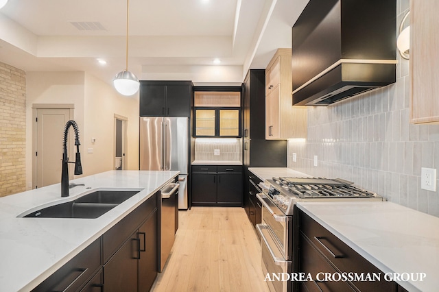 kitchen featuring premium appliances, sink, wall chimney exhaust hood, decorative light fixtures, and light hardwood / wood-style flooring