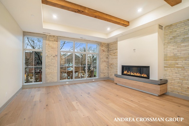 unfurnished living room featuring light hardwood / wood-style floors, brick wall, beam ceiling, and a raised ceiling