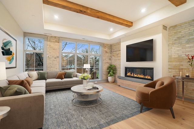 living room with beamed ceiling, a raised ceiling, hardwood / wood-style flooring, and brick wall