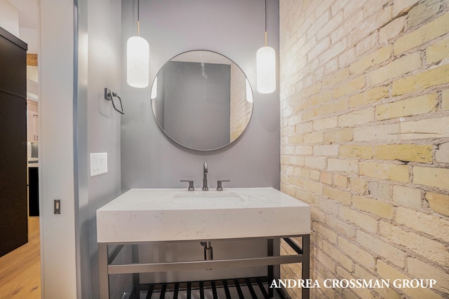 bathroom with brick wall, sink, and hardwood / wood-style floors