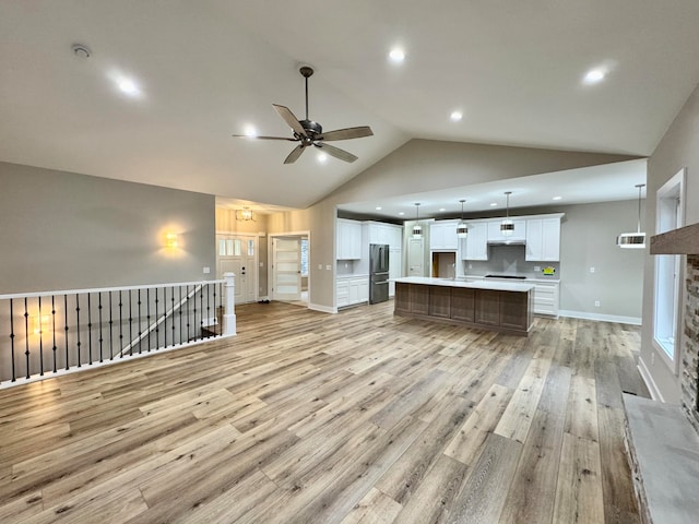 unfurnished living room featuring a stone fireplace, high vaulted ceiling, light wood-type flooring, and ceiling fan