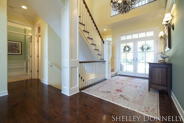 entrance foyer featuring crown molding, dark hardwood / wood-style flooring, french doors, a towering ceiling, and a chandelier