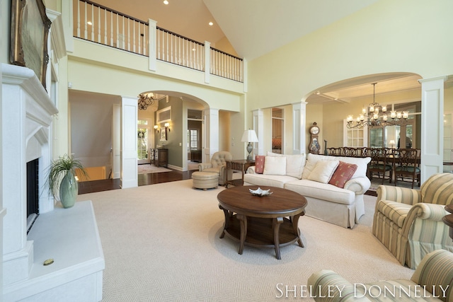 carpeted living room featuring decorative columns, high vaulted ceiling, and an inviting chandelier