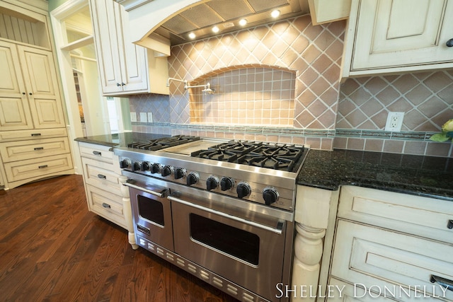 kitchen with decorative backsplash, premium range hood, range with two ovens, and dark stone counters