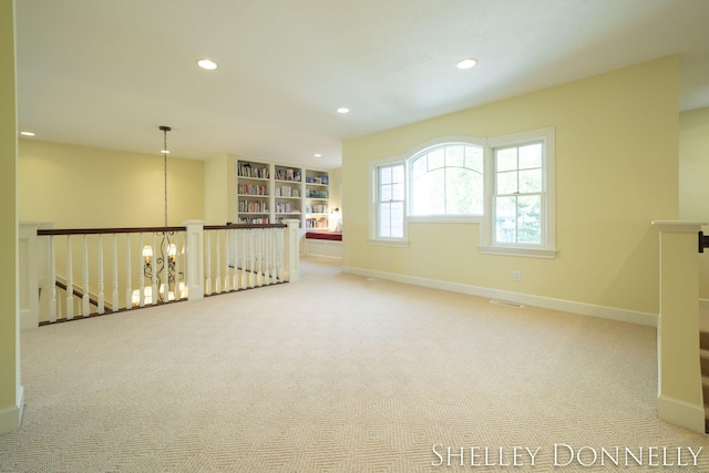 carpeted spare room with built in features and a chandelier