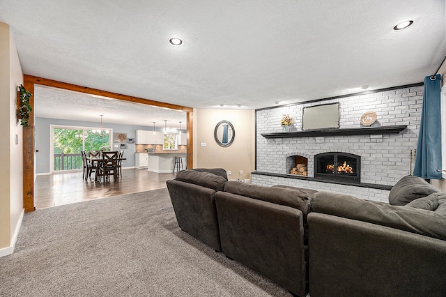 living area with carpet, a brick fireplace, a textured ceiling, wood finished floors, and baseboards