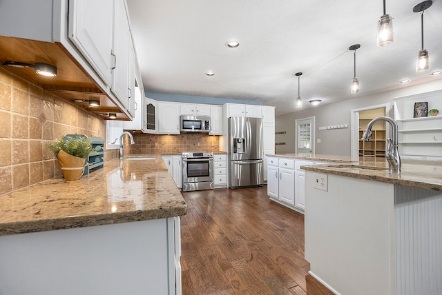 kitchen featuring light stone counters, stainless steel appliances, hanging light fixtures, white cabinetry, and a sink