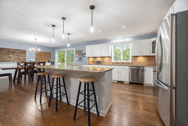 kitchen featuring a center island, stainless steel appliances, a kitchen bar, white cabinetry, and pendant lighting