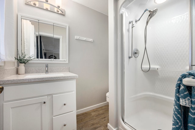 full bath with toilet, a stall shower, vanity, wood finished floors, and baseboards