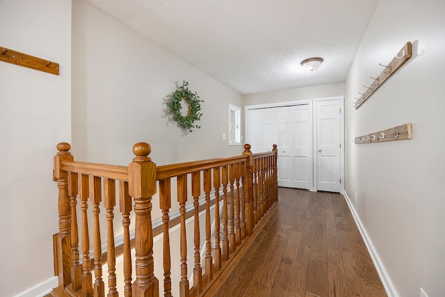 hallway featuring a textured ceiling, dark wood-style flooring, an upstairs landing, and baseboards