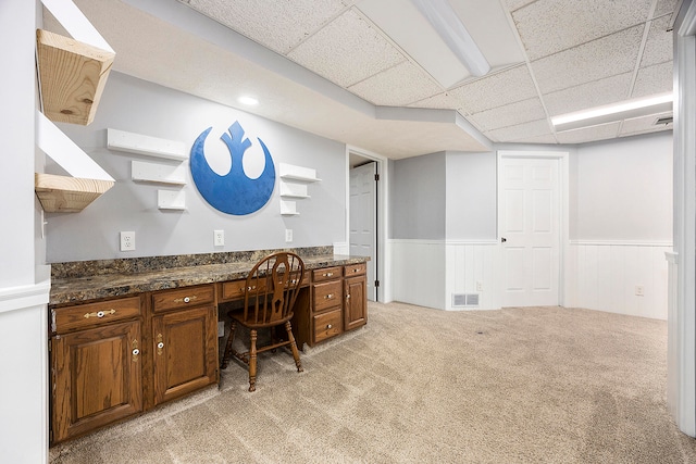 office space featuring visible vents, a drop ceiling, wainscoting, light colored carpet, and built in study area