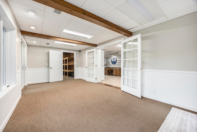 carpeted empty room featuring french doors, wainscoting, and a drop ceiling