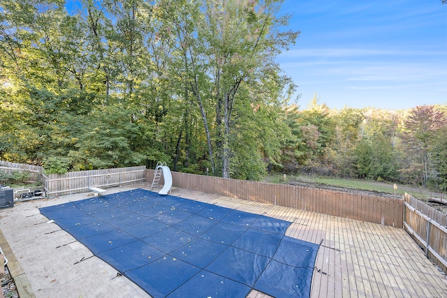 view of pool featuring a fenced in pool, central air condition unit, a water slide, a fenced backyard, and a diving board