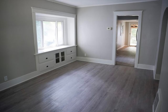 empty room with ornamental molding, plenty of natural light, and dark wood-type flooring