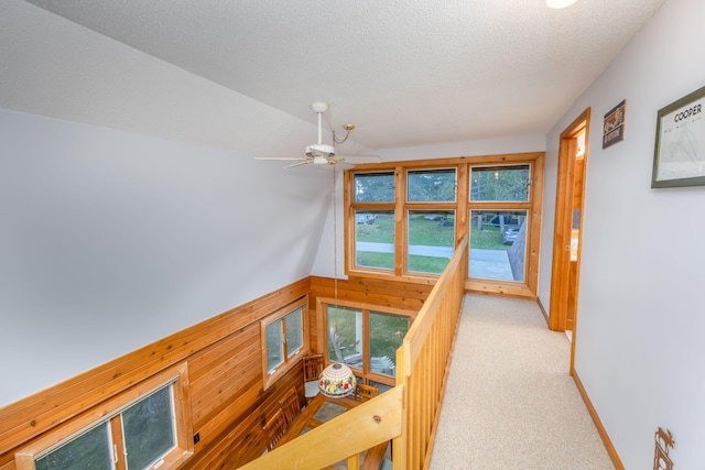 hall featuring a textured ceiling, wooden walls, and light colored carpet