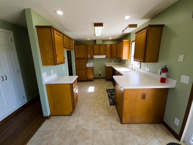 kitchen featuring a textured ceiling, kitchen peninsula, light tile patterned flooring, and sink