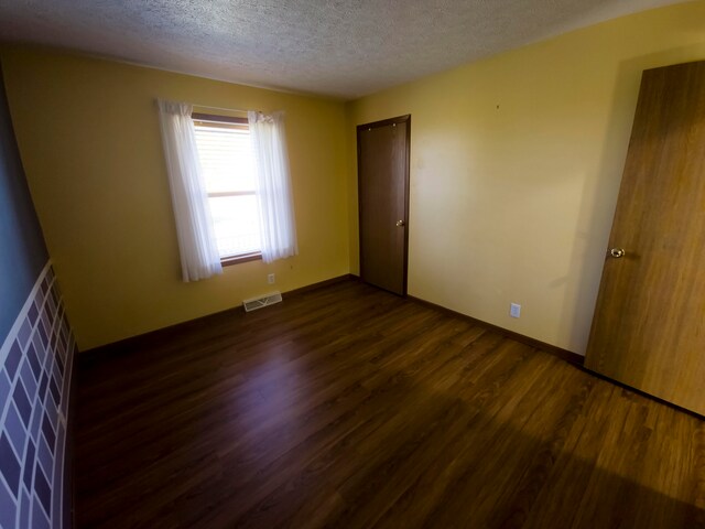 spare room featuring a textured ceiling and dark wood-type flooring