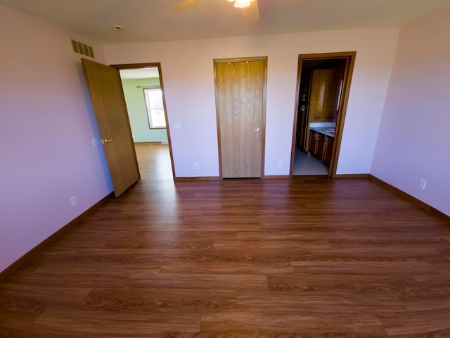 unfurnished bedroom with ceiling fan, ensuite bath, and dark wood-type flooring