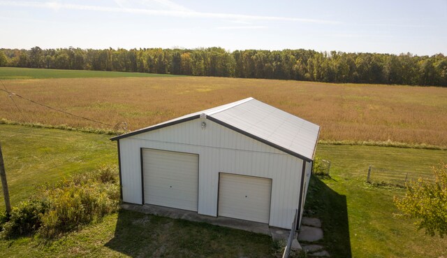 garage featuring a rural view, wood walls, and a lawn