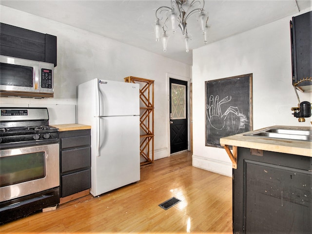 kitchen featuring appliances with stainless steel finishes, light wood-type flooring, a notable chandelier, and sink