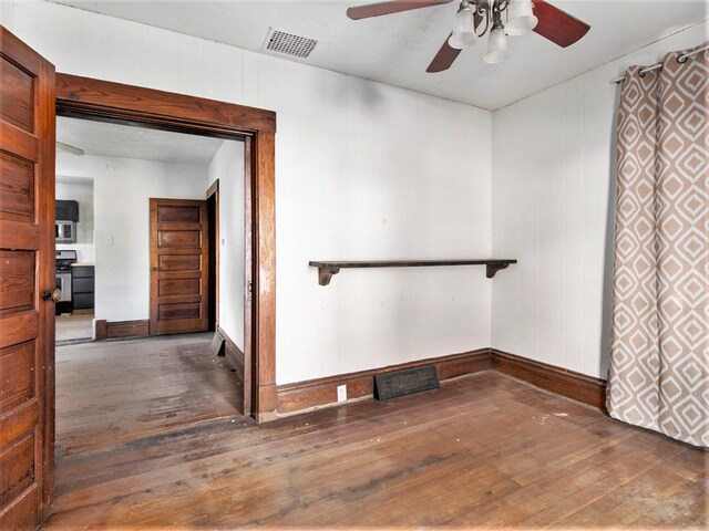 unfurnished room with wood walls, dark hardwood / wood-style floors, and ceiling fan