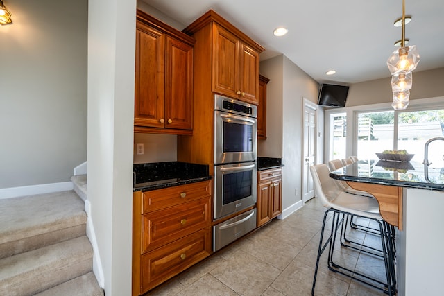 kitchen with pendant lighting, dark stone counters, a kitchen breakfast bar, double oven, and light tile patterned floors