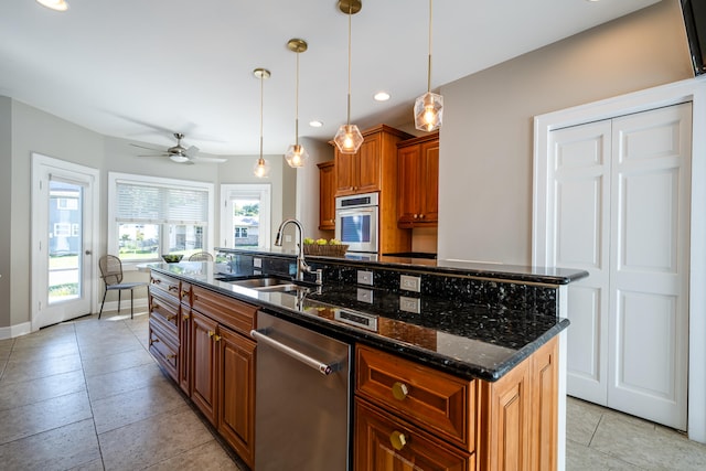 kitchen featuring a kitchen island with sink, dark stone countertops, sink, hanging light fixtures, and appliances with stainless steel finishes