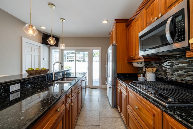 kitchen with pendant lighting, tasteful backsplash, dark stone countertops, sink, and stainless steel appliances