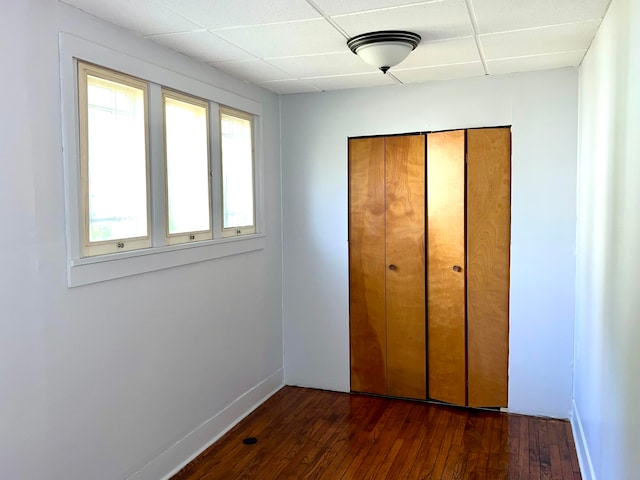 unfurnished bedroom with a closet, dark wood-type flooring, and a paneled ceiling