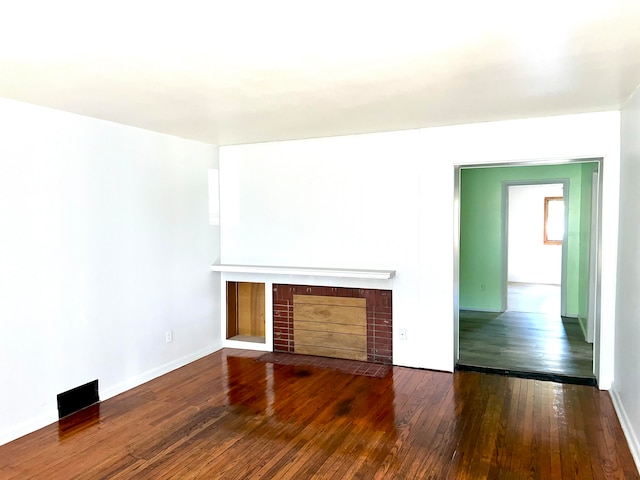 unfurnished living room featuring a brick fireplace and dark hardwood / wood-style floors