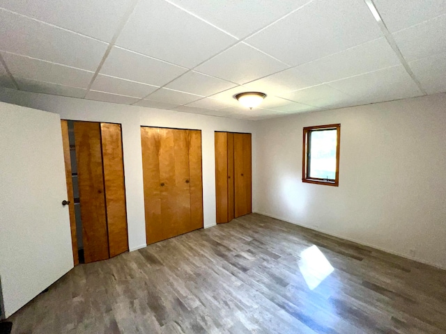 unfurnished bedroom with wood-type flooring, a drop ceiling, and two closets