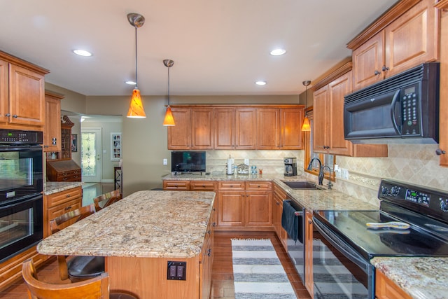 kitchen featuring light stone counters, black appliances, a center island, a breakfast bar area, and light hardwood / wood-style flooring