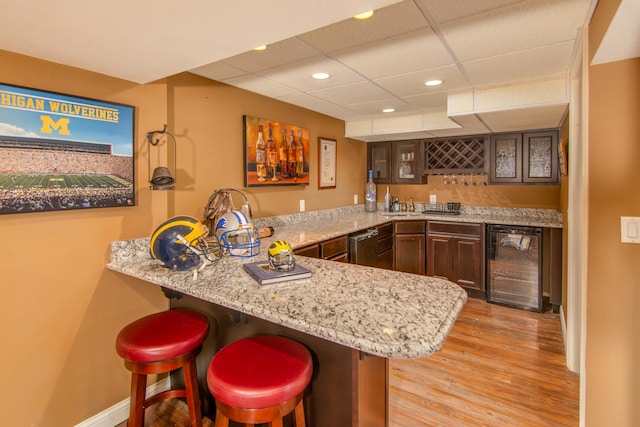 bar featuring wine cooler, light wood-type flooring, dark brown cabinets, dishwasher, and light stone countertops