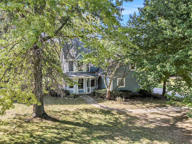 view of property hidden behind natural elements featuring a front lawn and a porch