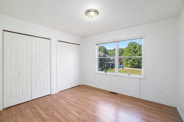 unfurnished bedroom featuring light hardwood / wood-style flooring and two closets