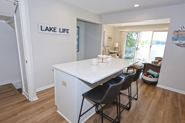 kitchen with dark wood-type flooring, a breakfast bar area, a kitchen island, and light stone counters