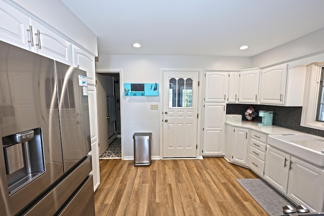 kitchen featuring decorative backsplash, wood-type flooring, stainless steel refrigerator with ice dispenser, and white cabinetry