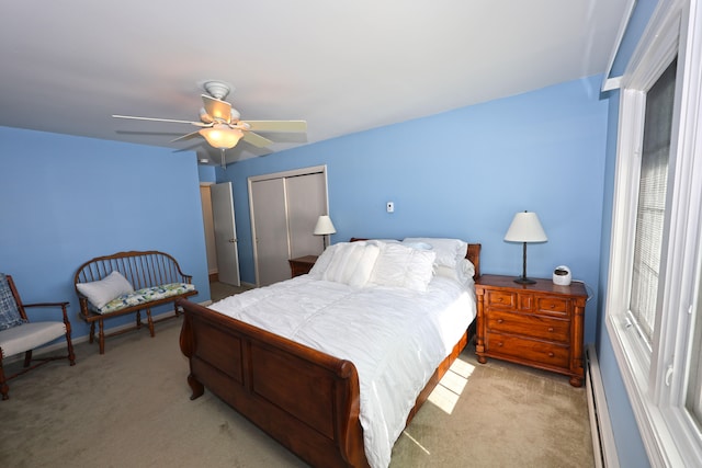 bedroom with baseboard heating, ceiling fan, a closet, and light colored carpet