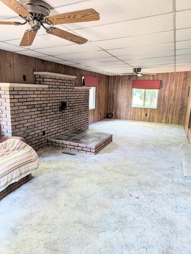 unfurnished living room with carpet floors, a drop ceiling, wood walls, and ceiling fan