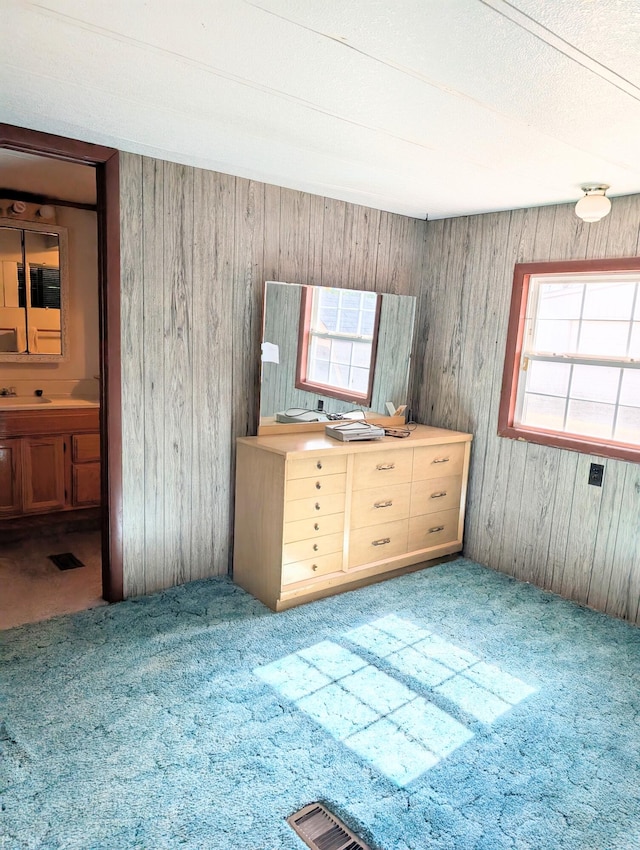 unfurnished bedroom featuring multiple windows, carpet, wooden walls, and sink