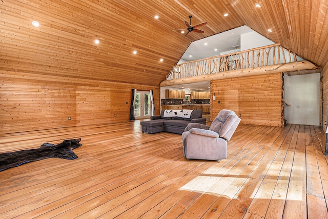 living room with light hardwood / wood-style flooring, wood walls, and high vaulted ceiling