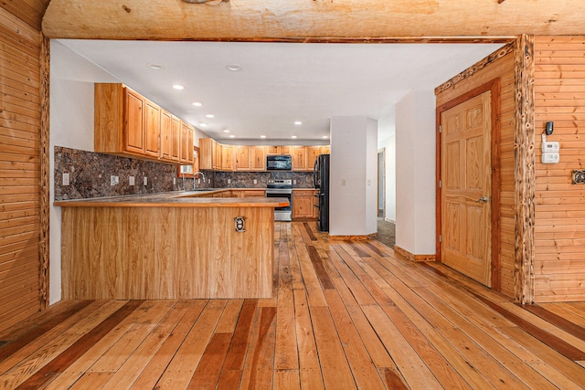 kitchen with light hardwood / wood-style floors, kitchen peninsula, wood walls, and black appliances